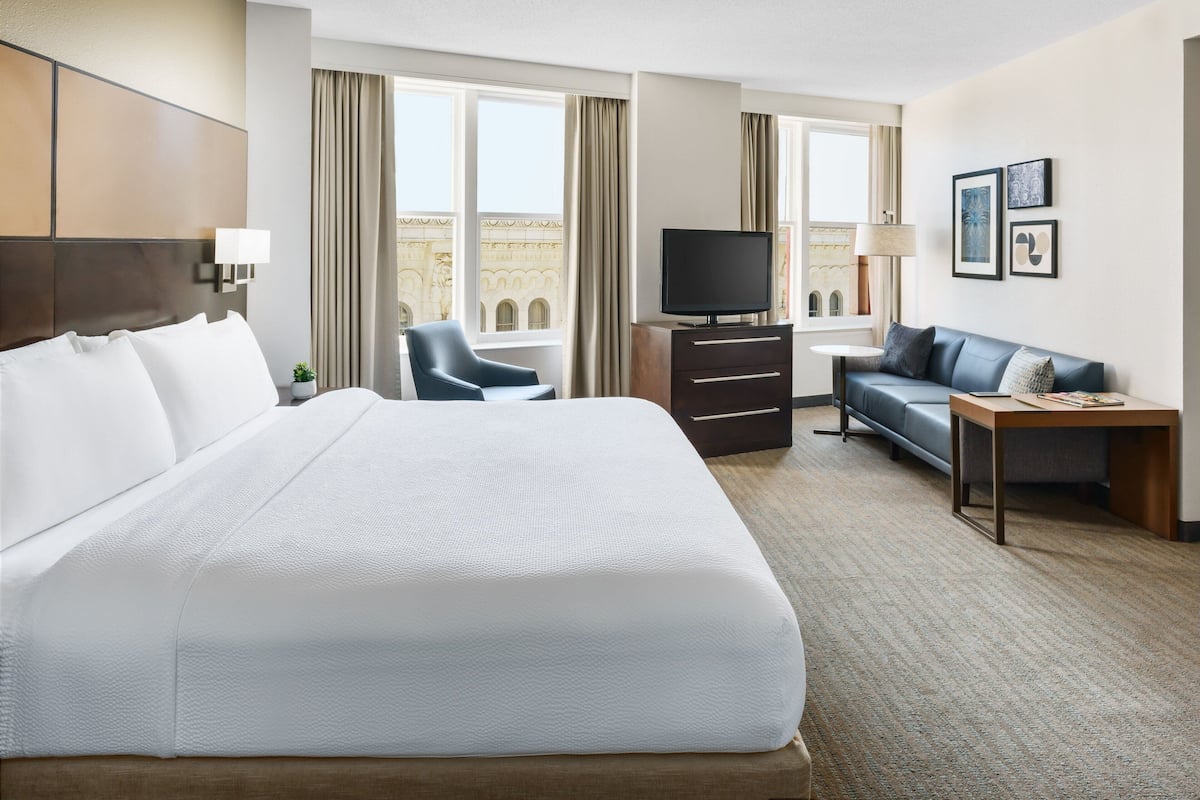 A hotel room with a large bed, a desk, a chair, a television, and a sofa.