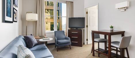 Une chambre d’hôtel moderne avec un canapé bleu, une petite table ronde, un téléviseur et un bureau avec deux chaises.