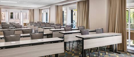 A conference room with multiple tables and chairs, large windows with curtains, and a patterned carpet.