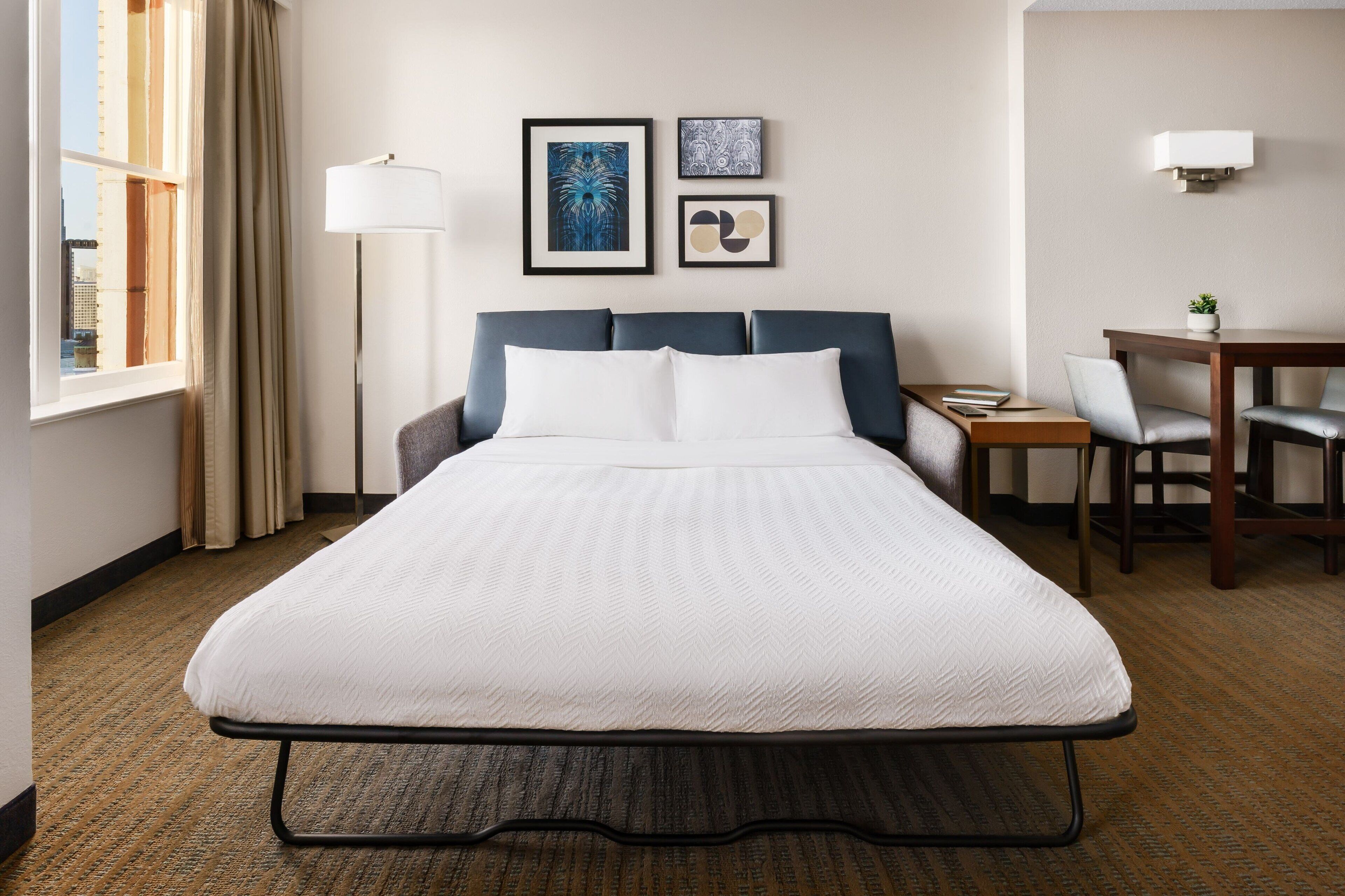 Ein Hotelzimmer mit Bett, Schreibtisch und Stuhl. An der Wand hängen gerahmte Bilder.
