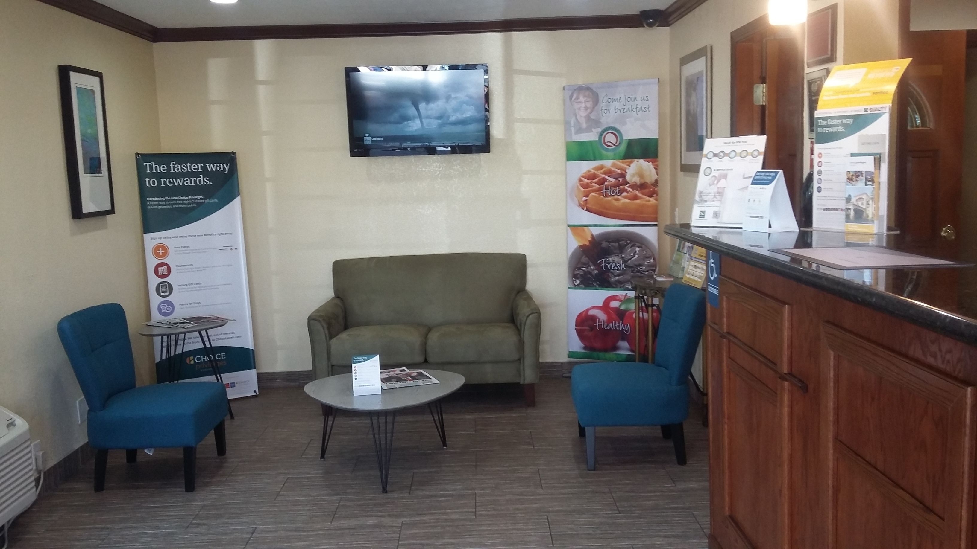 A lobby with a sofa, two chairs, a small table, a TV on the wall, and a reception desk.