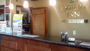 A hotel reception desk with a wooden counter, a sign reading "Quality Inn by Choice Hotels," and a reception area with a window and blinds. - Quality Inn San Diego I-5 Naval Base (San Diego)