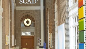 Un vaste couloir agrémenté d’un grand lustre, d’une horloge et d’une enseigne indiquant « SCAD ».