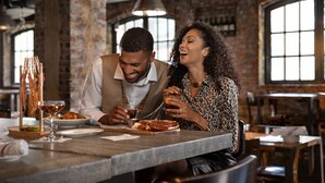 Un couple est assis à une table dans un restaurant dont l’intérieur est décoré de briques apparentes et qui possède de grandes fenêtres.