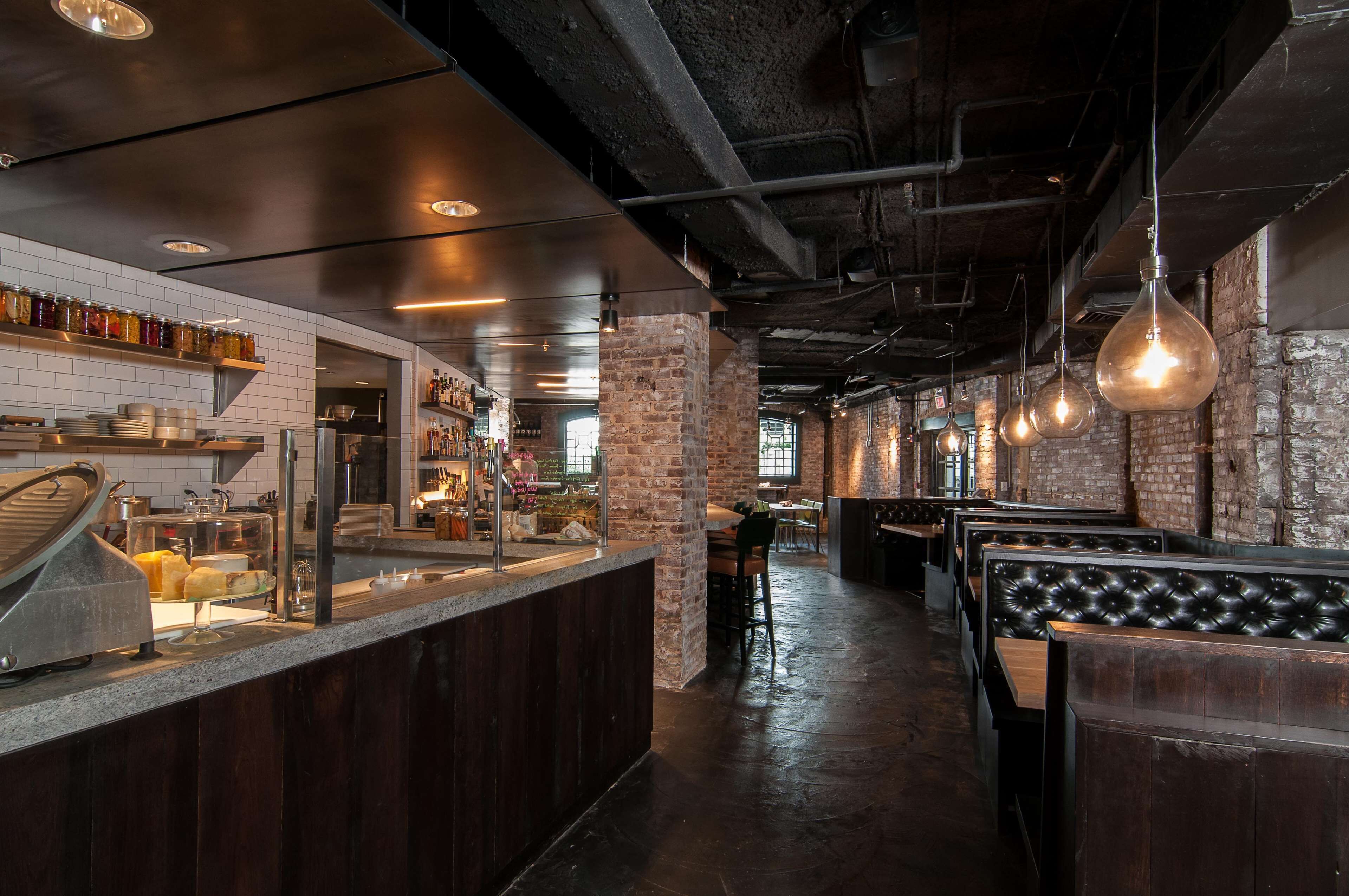 A restaurant interior with brick walls, wooden benches, a counter with food items, and hanging light fixtures.