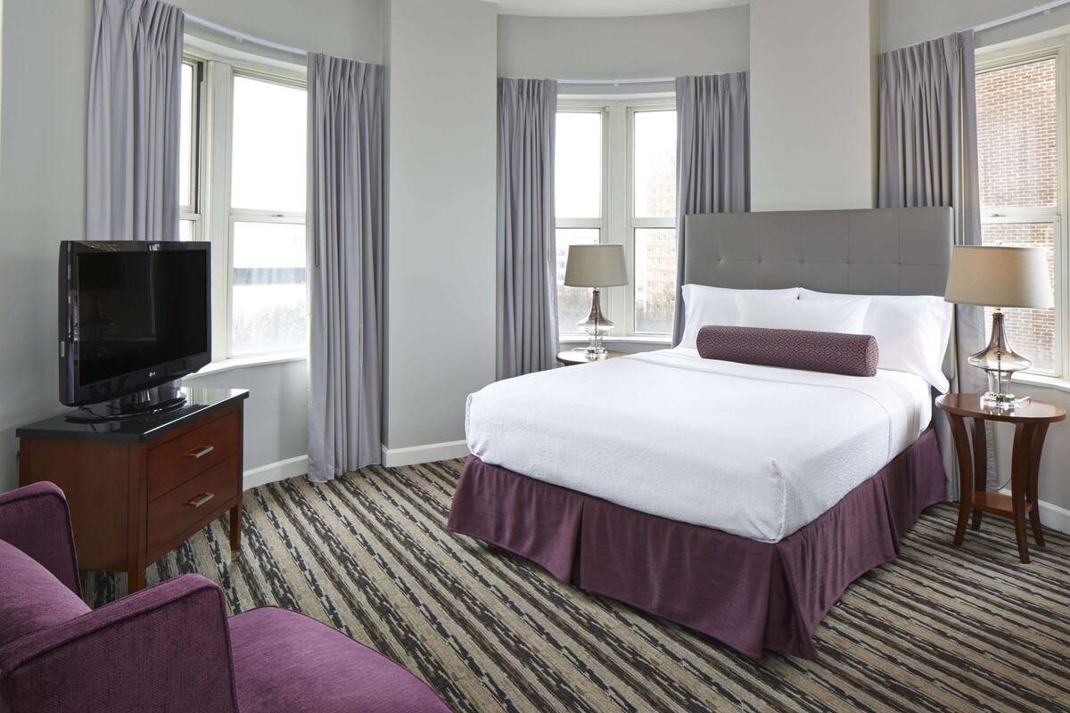 A hotel room with a bed, a TV, a desk, and a chair.