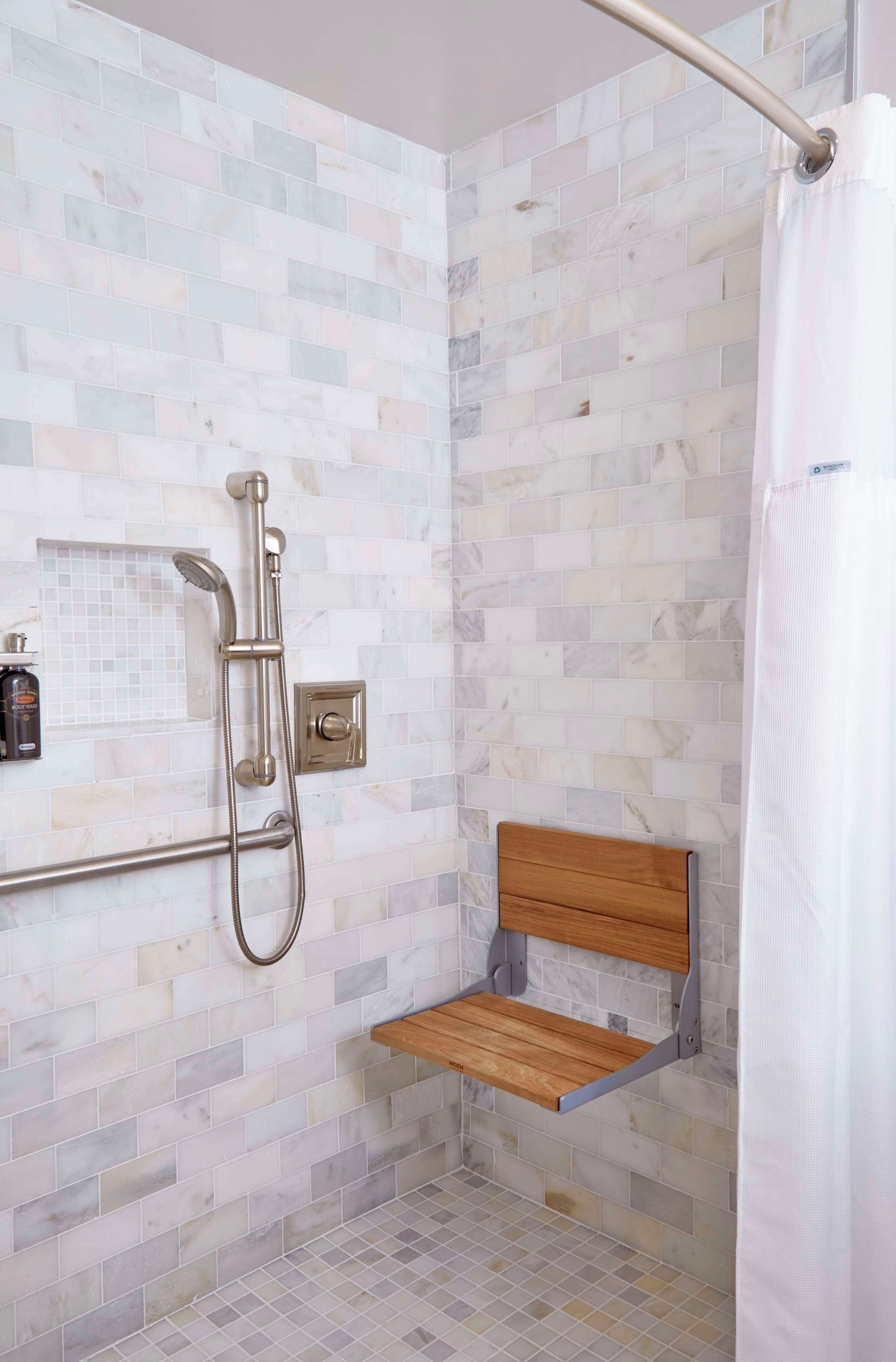 Un área de ducha con una barra de apoyo, un banco de madera y un muro revestido de azulejos.