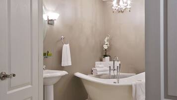 A bathroom with a freestanding bathtub, a pedestal sink, and a chandelier.