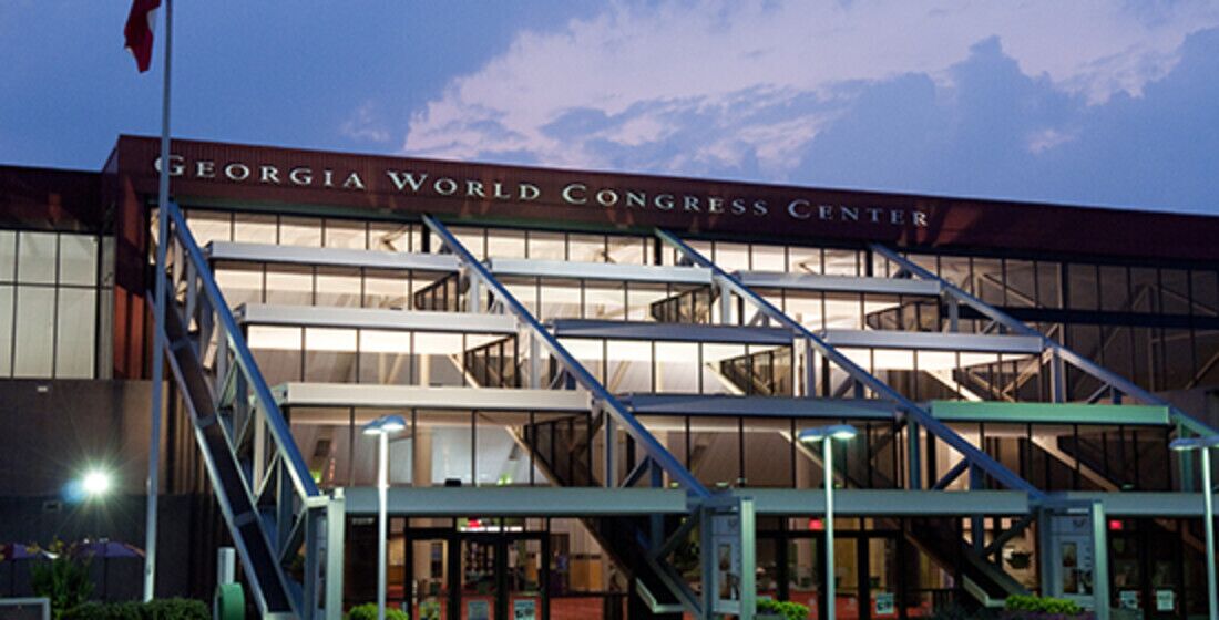 The Georgia World Congress Center with a modern architectural design, featuring a prominent entrance with glass doors and a staircase leading to the upper levels.