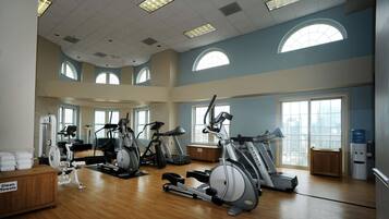 A spacious gym with multiple exercise machines, large windows, and a clean, well-lit environment.