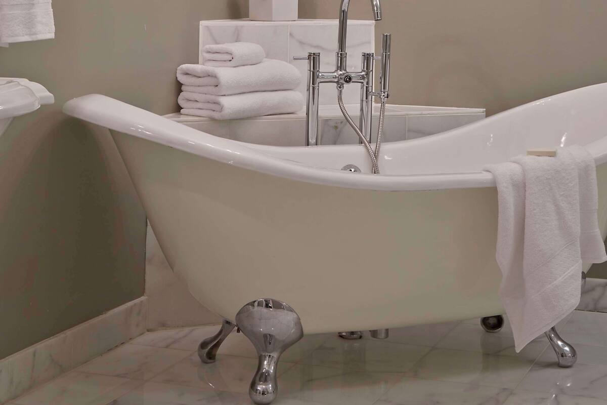 A bathroom with a freestanding bathtub, a modern chandelier, and a potted orchid.