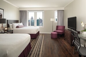 A hotel room with two beds, a desk with a TV, a chair, a dresser, and a view of the cityscape.