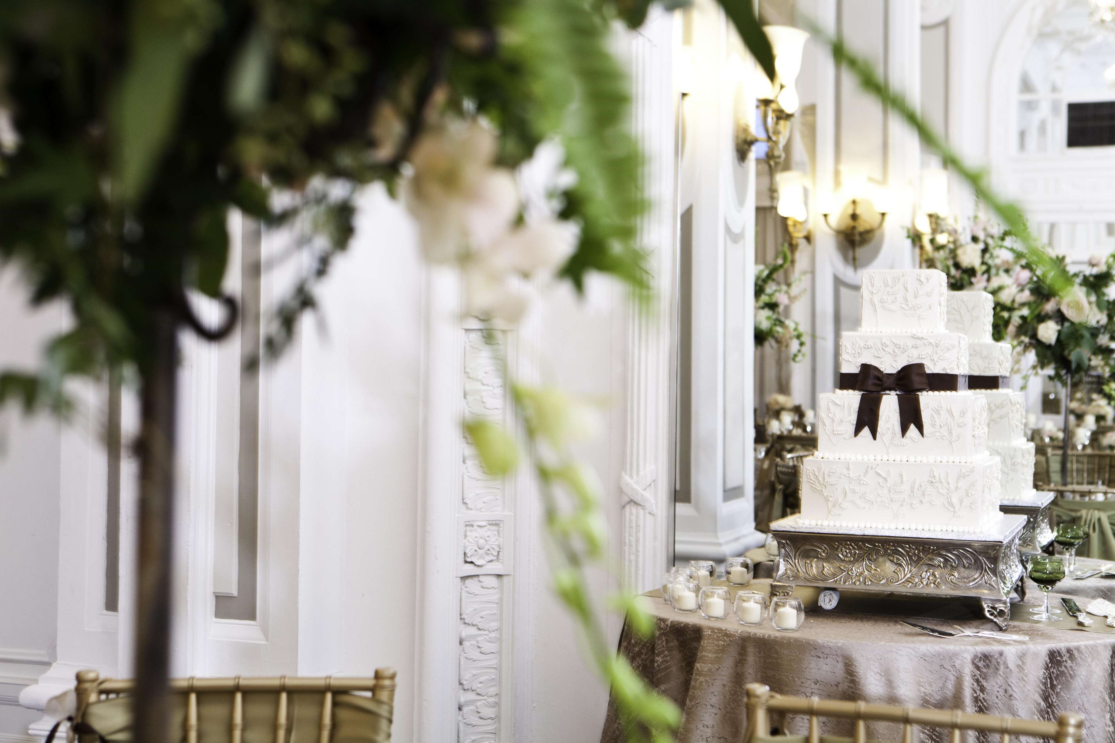 A three-tiered white cake with black ribbons on a table, surrounded by candles and greenery.
