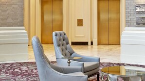 Un hall d’entrée agrémenté d’un magnifique lustre, de deux ascenseurs et d’un espace détente avec un tapis à motifs.