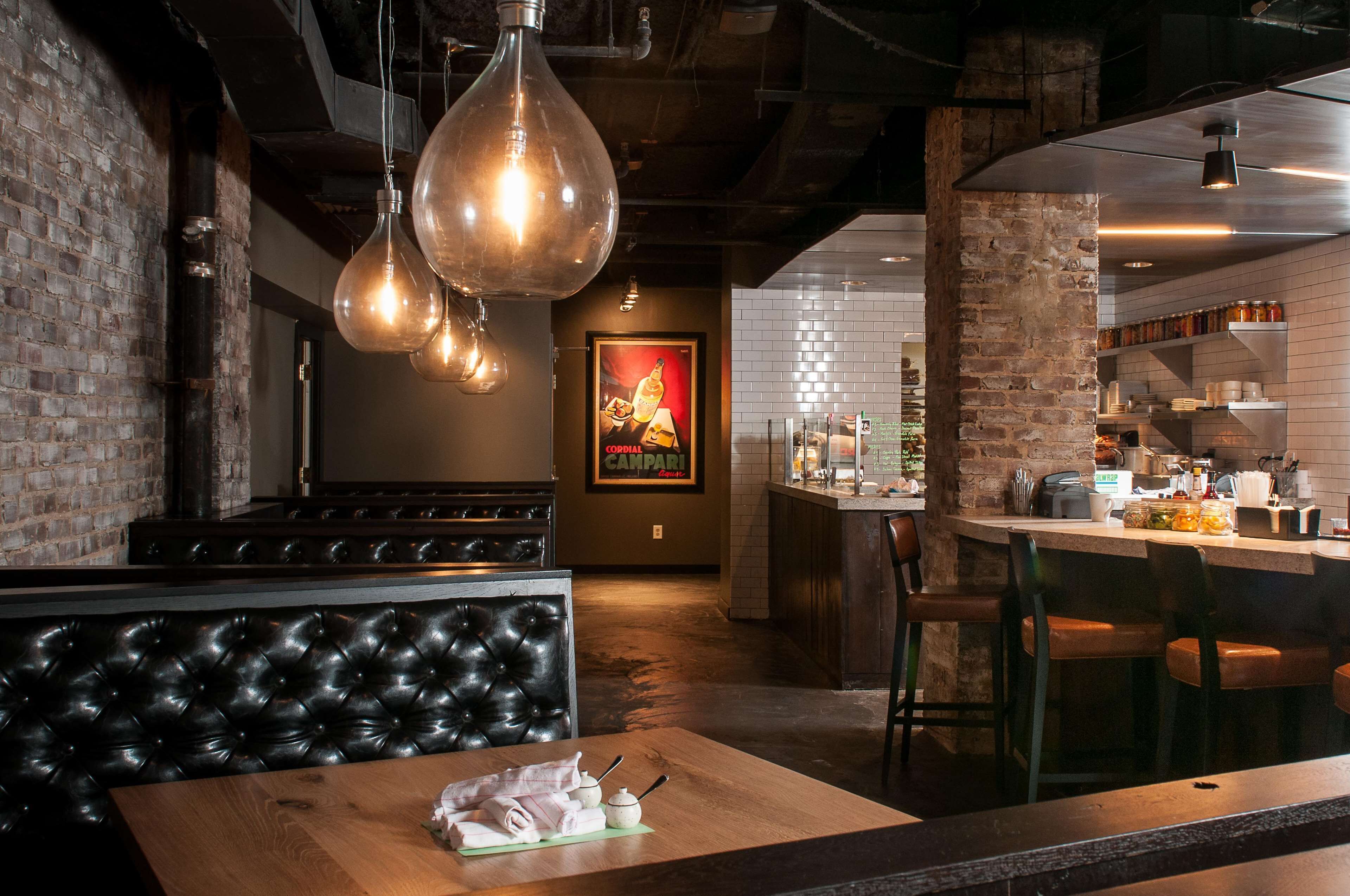 A restaurant with a brick wall, hanging light fixtures, a bar area, and a poster on the wall.