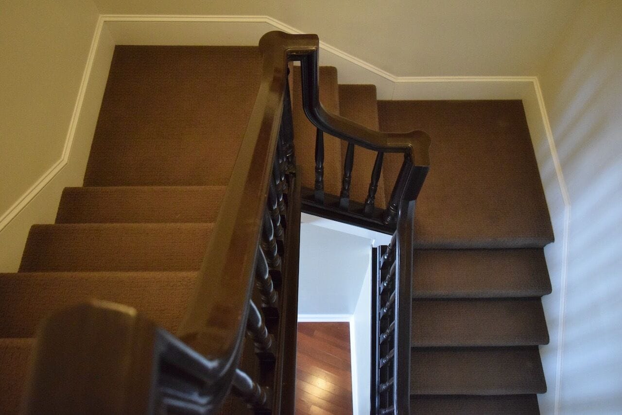 A staircase with a wooden handrail and brown carpeted steps.