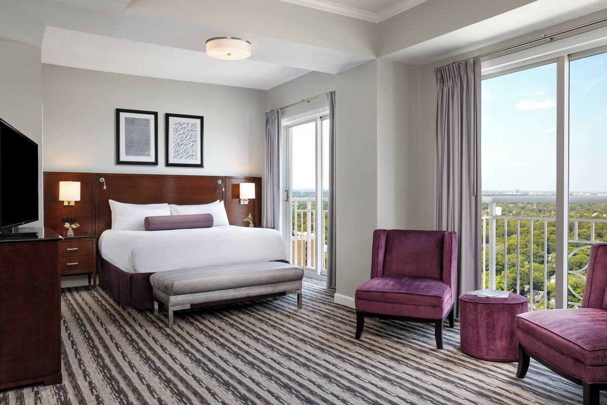 A hotel room with a large bed, a TV, a desk, and a view of the city.