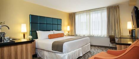 Habitación de hotel con una cama grande, un escritorio, una silla, un televisor y una ventana con cortinas.