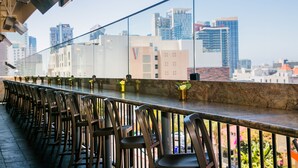 A rooftop bar with rows of chairs and tables, overlooking a cityscape with high-rise buildings.