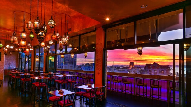 A restaurant with multiple tables and chairs, large windows, and hanging lanterns.