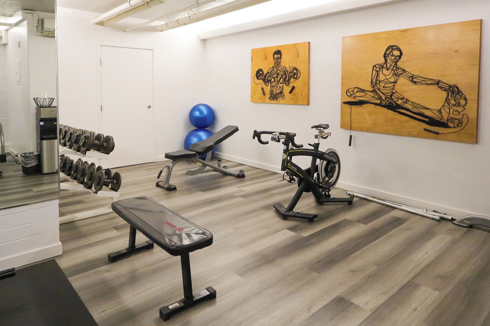 Ein Fitnessraum mit Trainingsgeräten, einer Bank und zwei Holzskulpturen an der Wand.