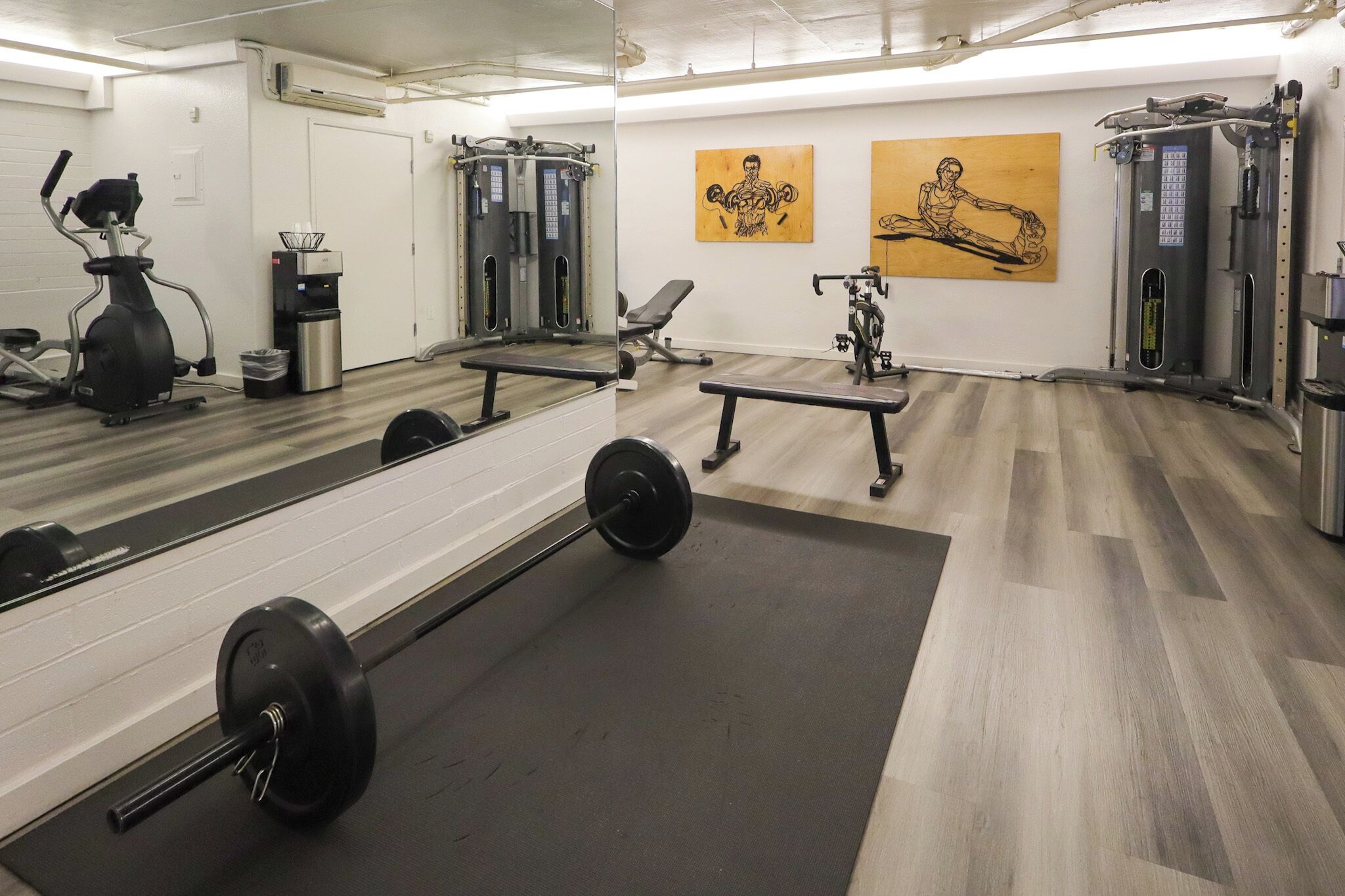 Ein Fitnessraum mit Trainingsgeräten, einem Spiegel und Kunstwerken an den Wänden.