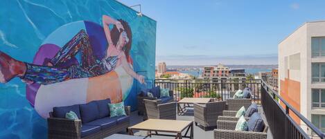 Terraço no telhado com mobiliário de vime, um mural e vista para a cidade.