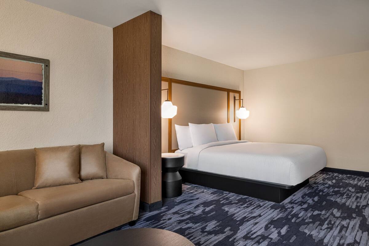 A hotel room with a bed, a sofa, a nightstand, and a painting on the wall.