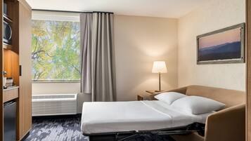 A hotel room with a bed, a desk, a lamp, a window with curtains, and a painting on the wall.