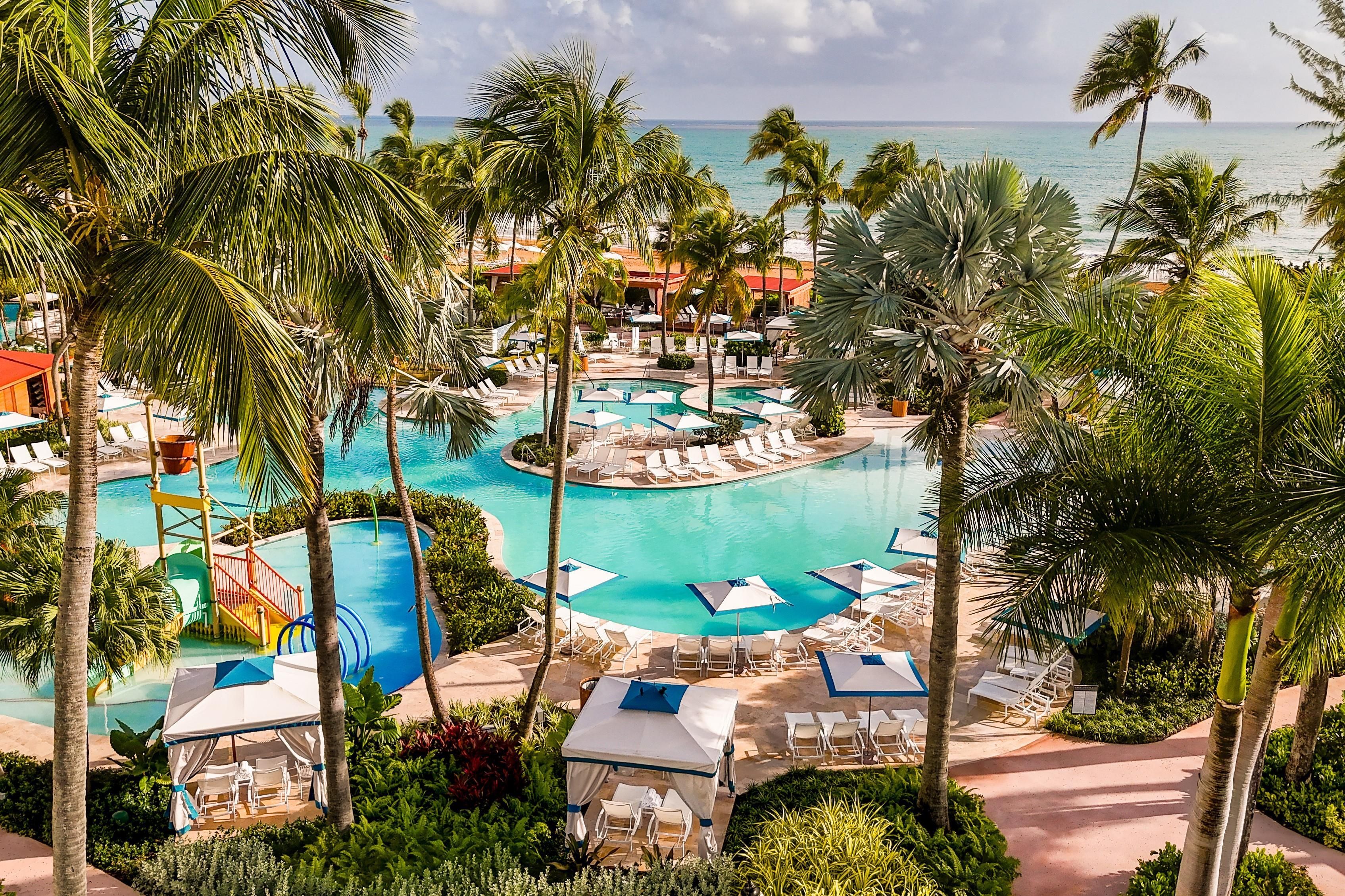 A resort with a central pool, lounge areas, and a view of the ocean.