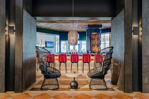 A lobby with two black wireframe chairs, a round table, and a bar area with red chairs.