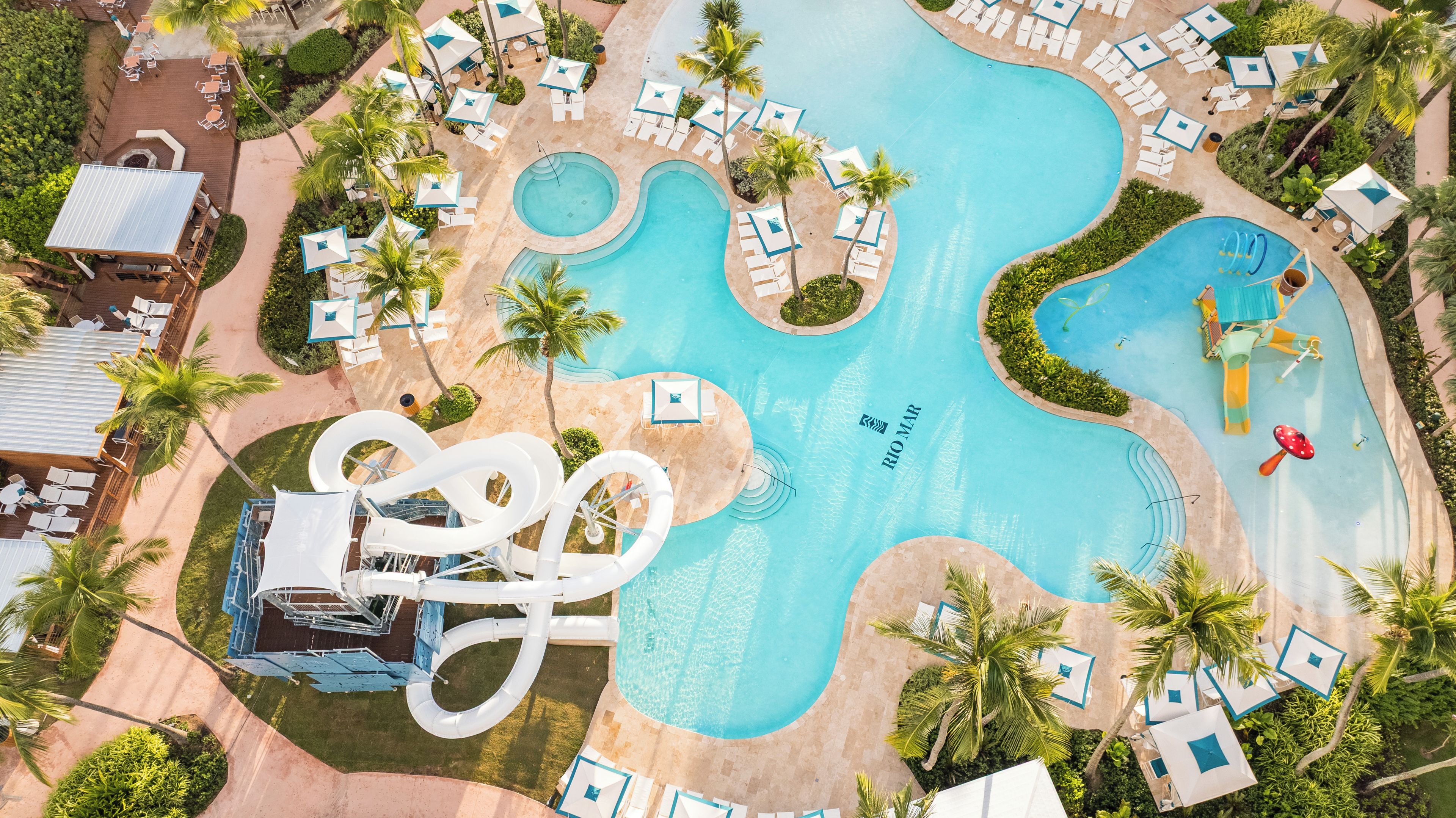 Un complexe hôtelier doté de plusieurs piscines, d’un toboggan aquatique et d’espaces de détente avec des parasols.