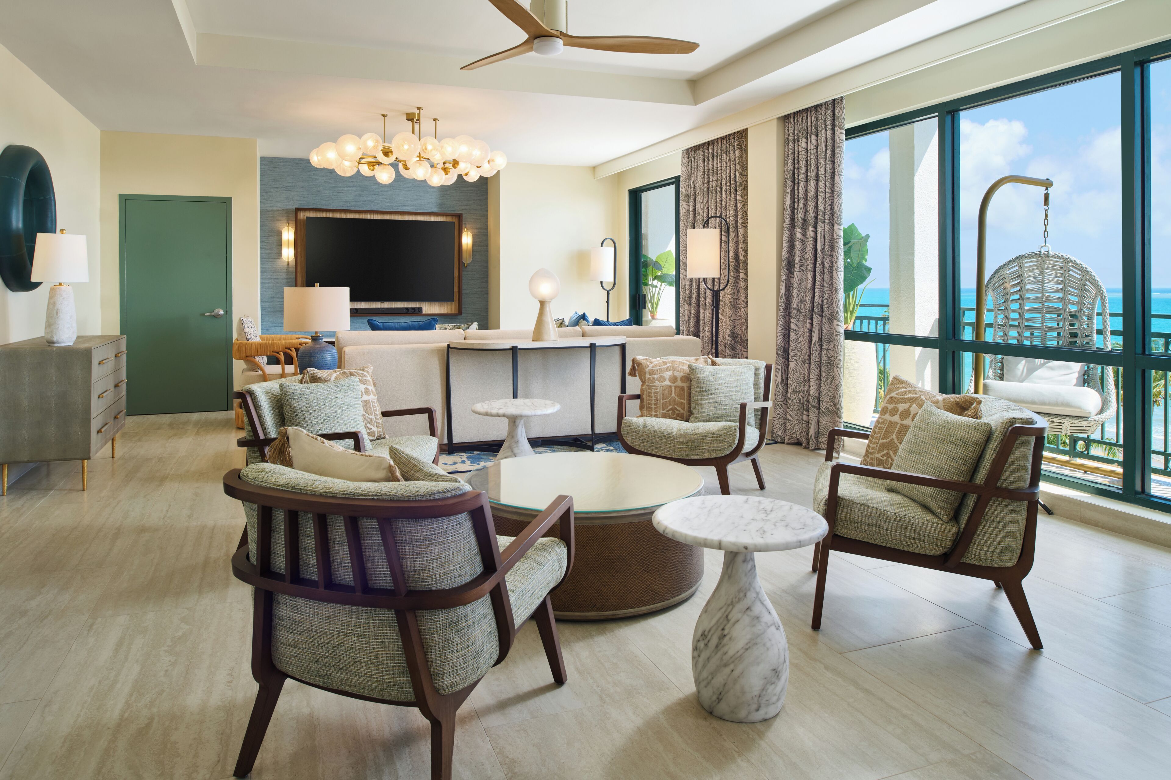 A modern hotel room with a seating area, a flat-screen TV, a dining table, and a view of the ocean.