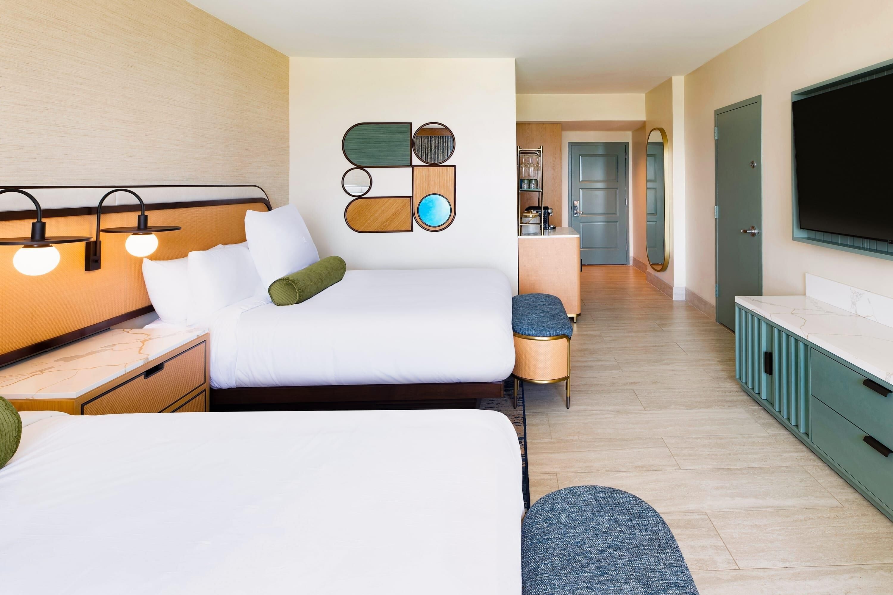 A hotel room with a bed, bedside tables, a TV, and a kitchenette.