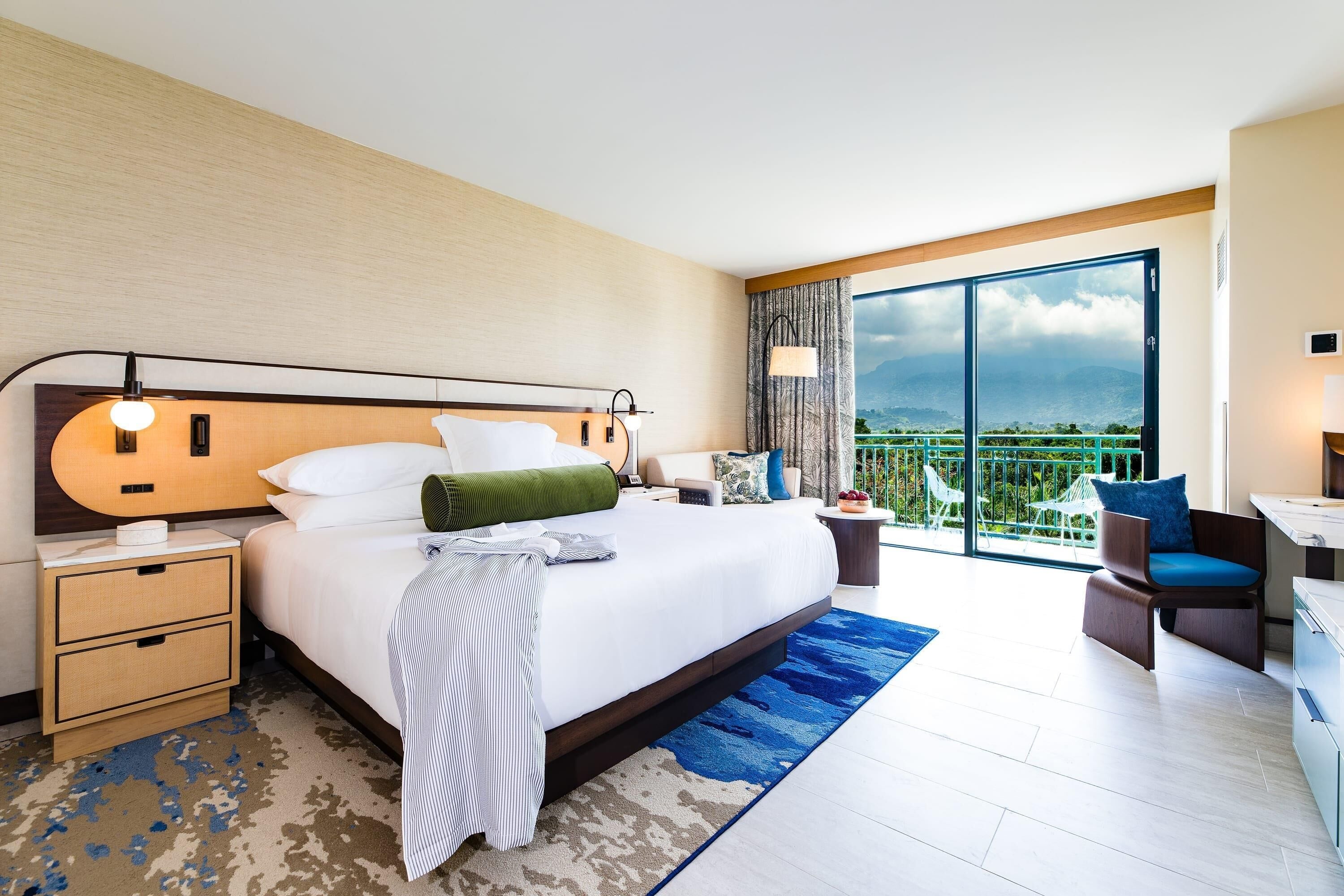 A hotel room with a large bed, a desk, a chair, and a balcony with a view.