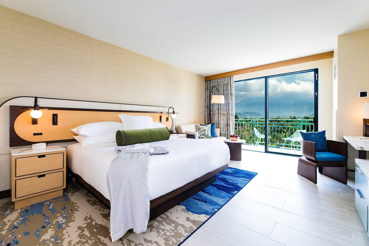 A hotel room with a large bed, a desk, a chair, and a balcony with a view.