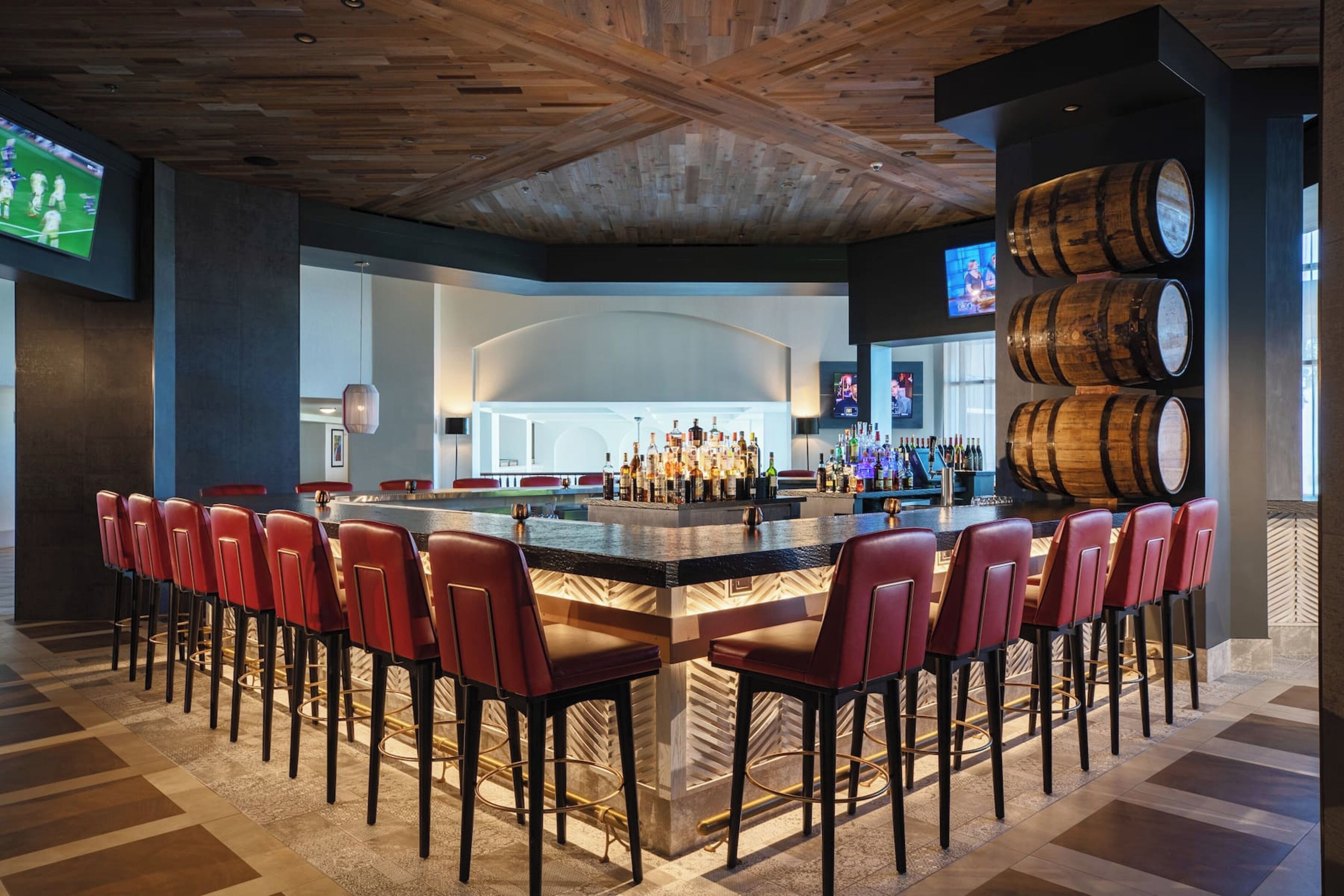 Una zona de bar con una barra larga, sillas rojas y barriles de madera.
