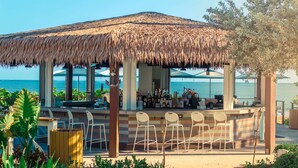A beachside bar with a thatched roof, outdoor seating, and a view of the ocean. - Wyndham Grand Rio Mar Rainforest Beach and Golf Resort (Río Grande)