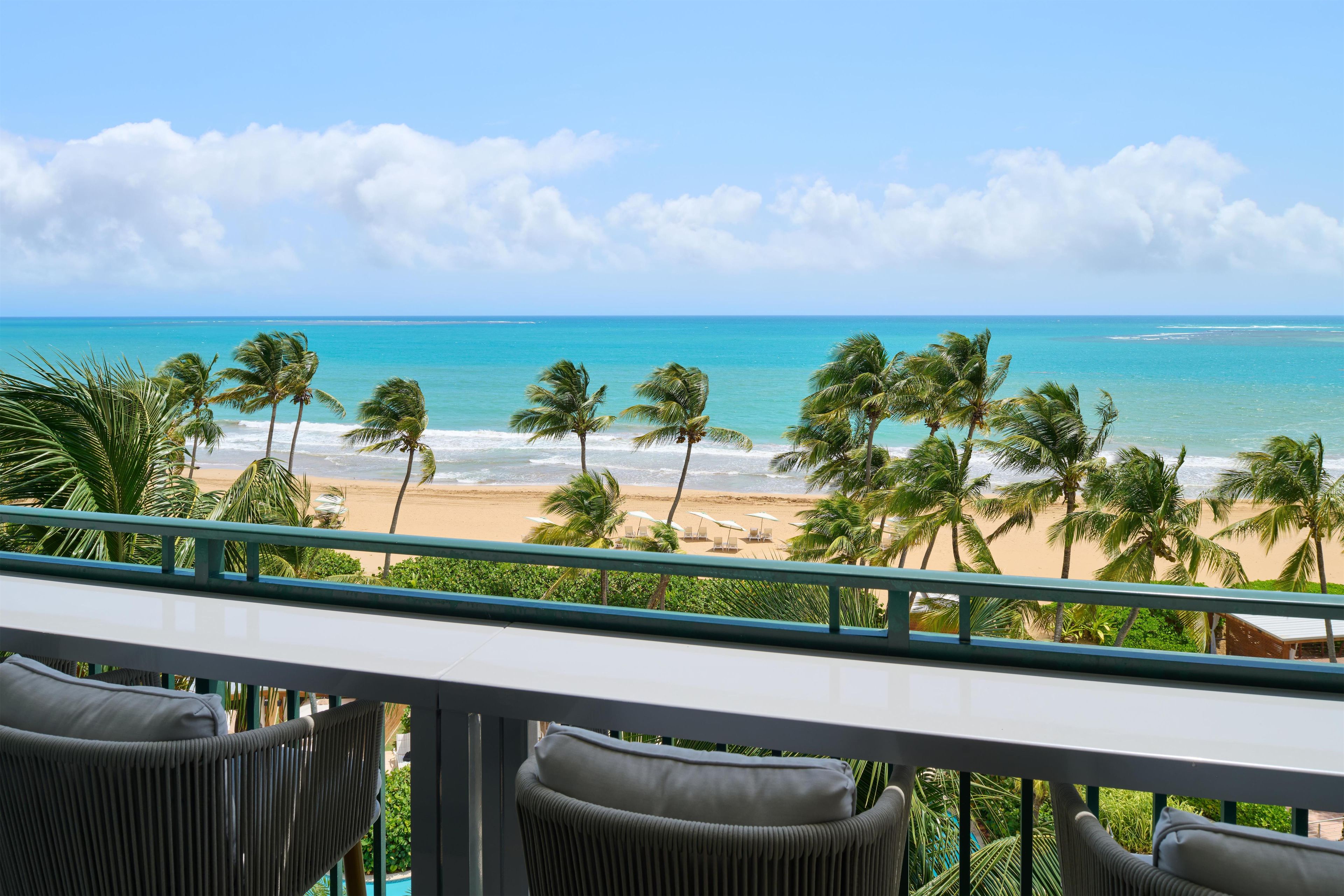 Un balcon avec vue sur une plage, des palmiers et l’océan.