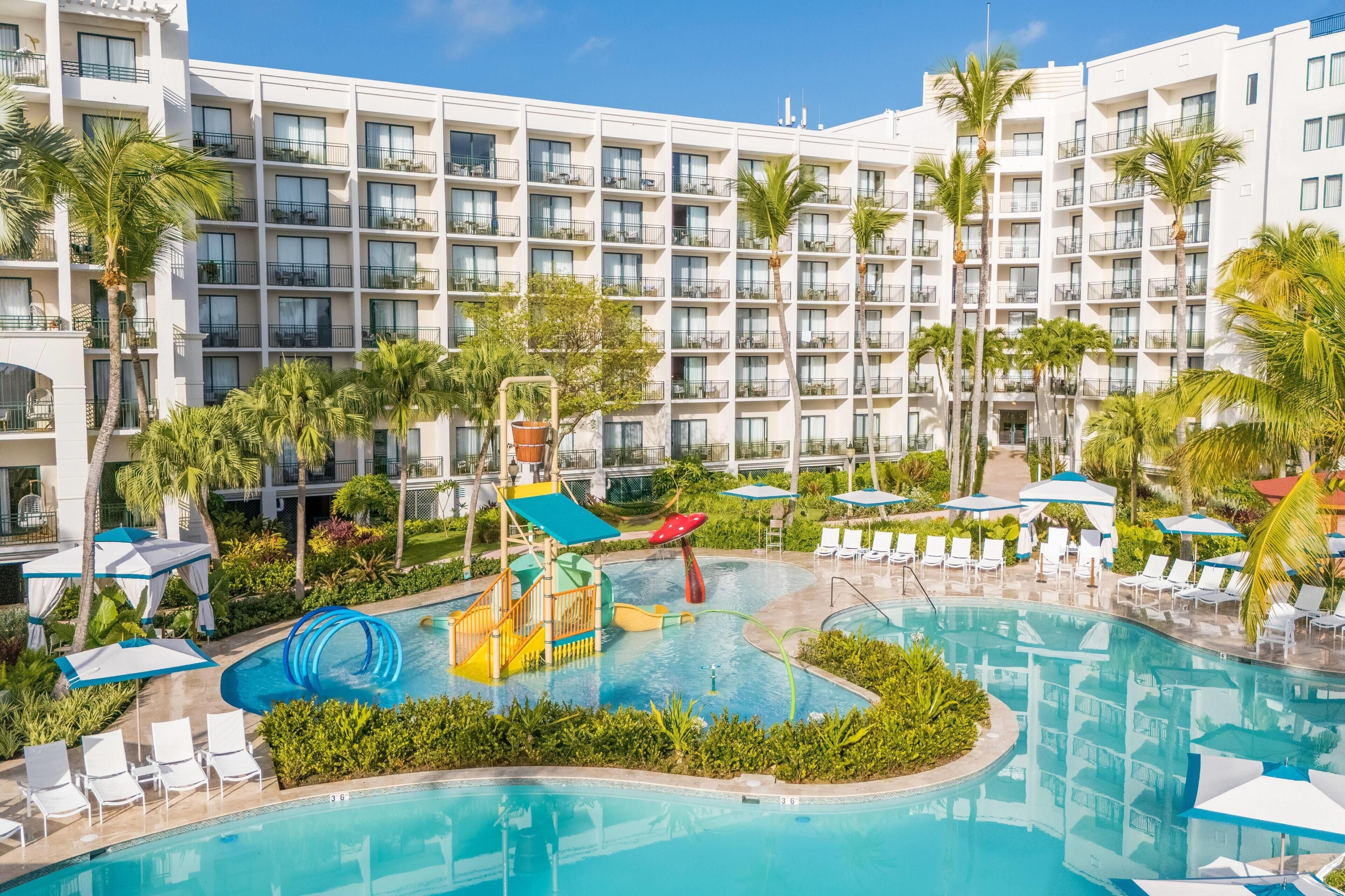 A hotel with a large pool, palm trees, and a water slide.