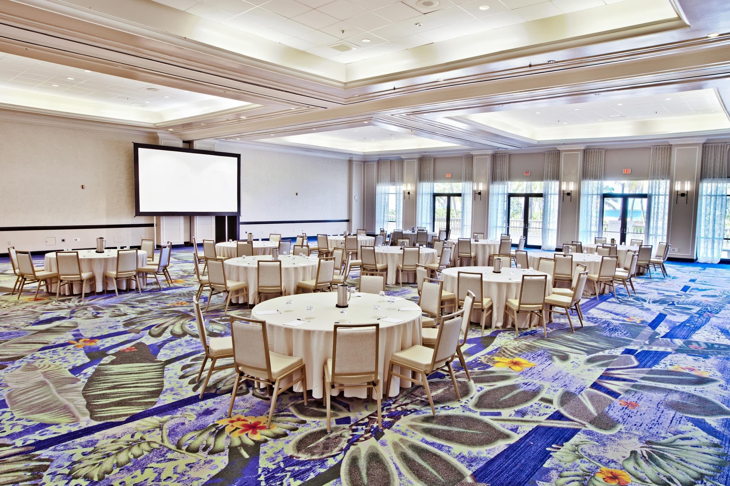 A conference room with round tables, chairs, a projector screen, and large windows.