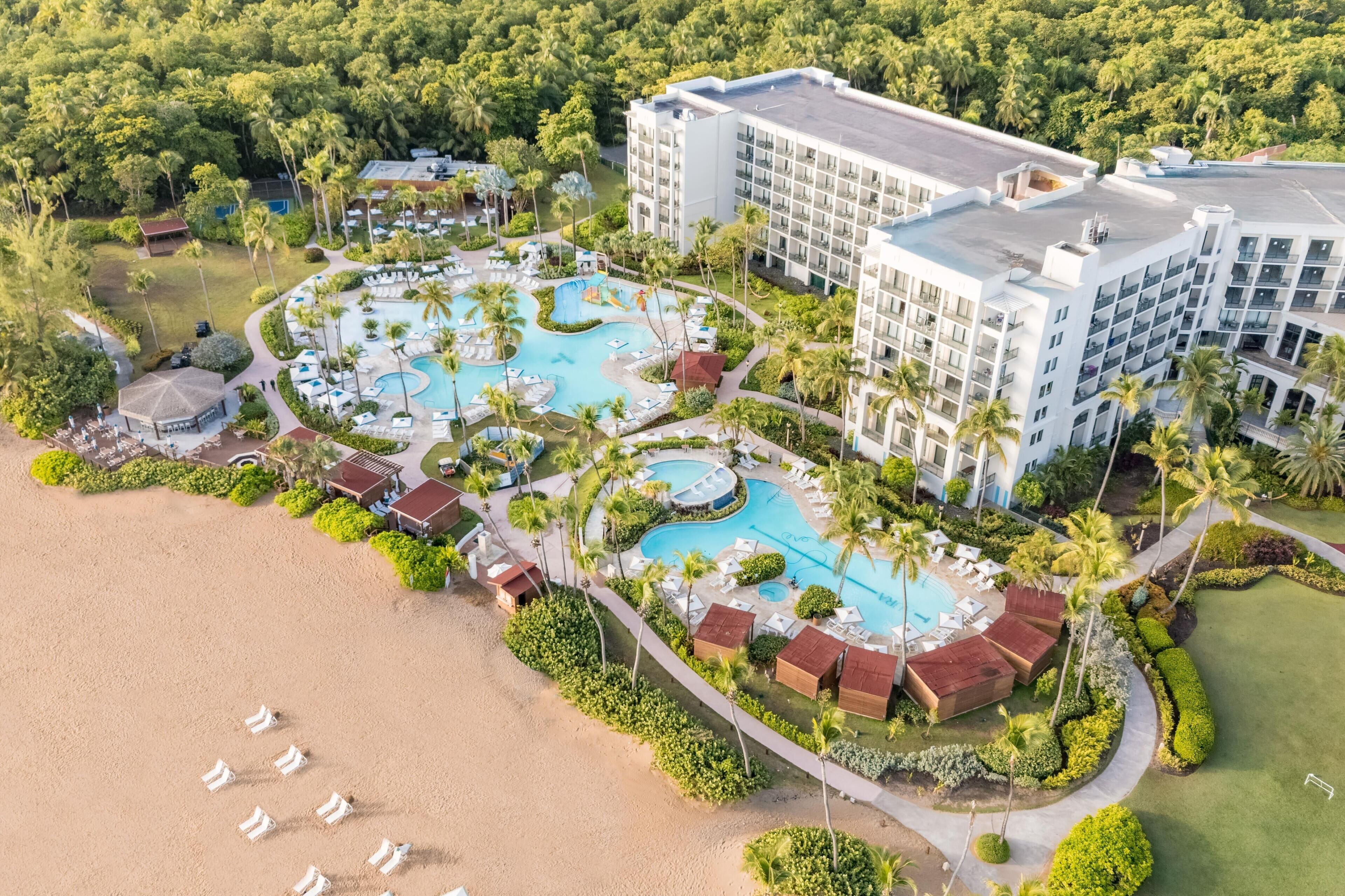 Et resort med flere swimmingpools, en strand og en stor hotelbygning.