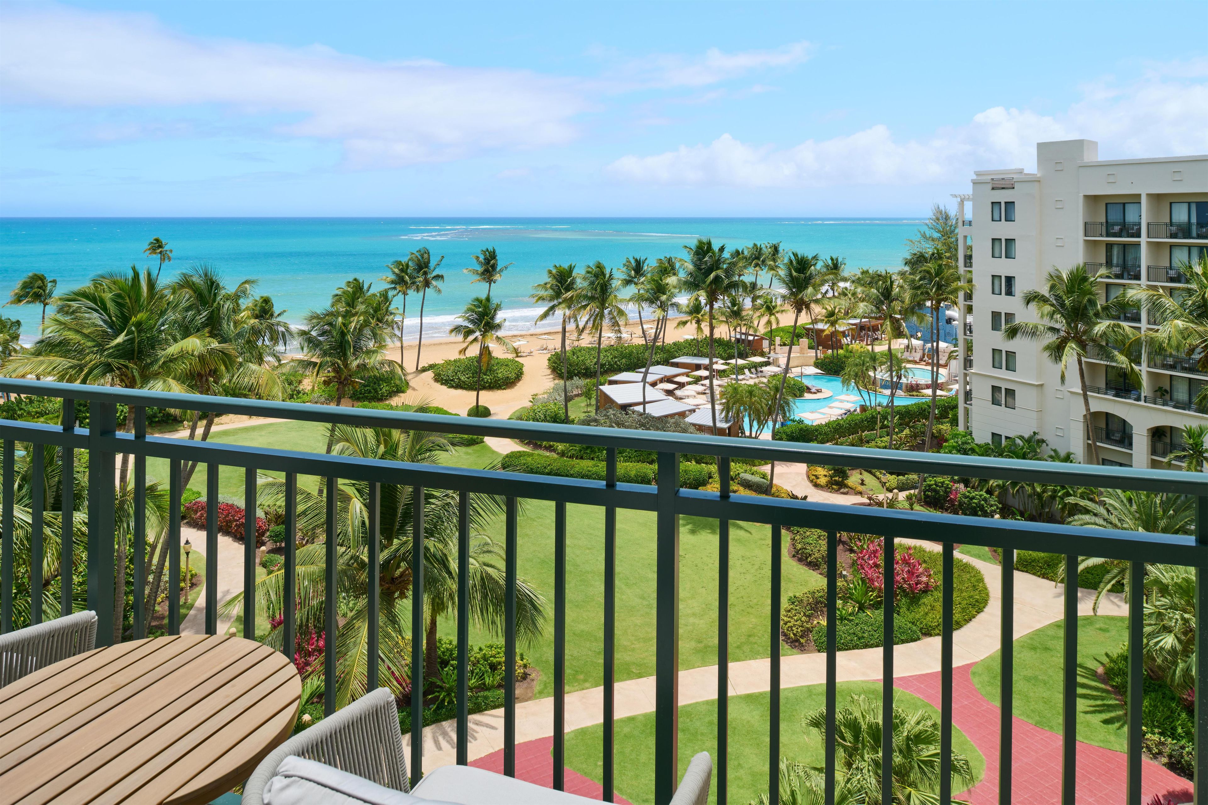 A balcony with a view of a beach, pool, and hotel building.