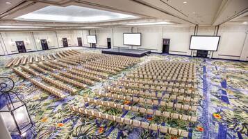 Un salón de conferencias amplio con filas de sillas, un escenario y una pantalla grande.
