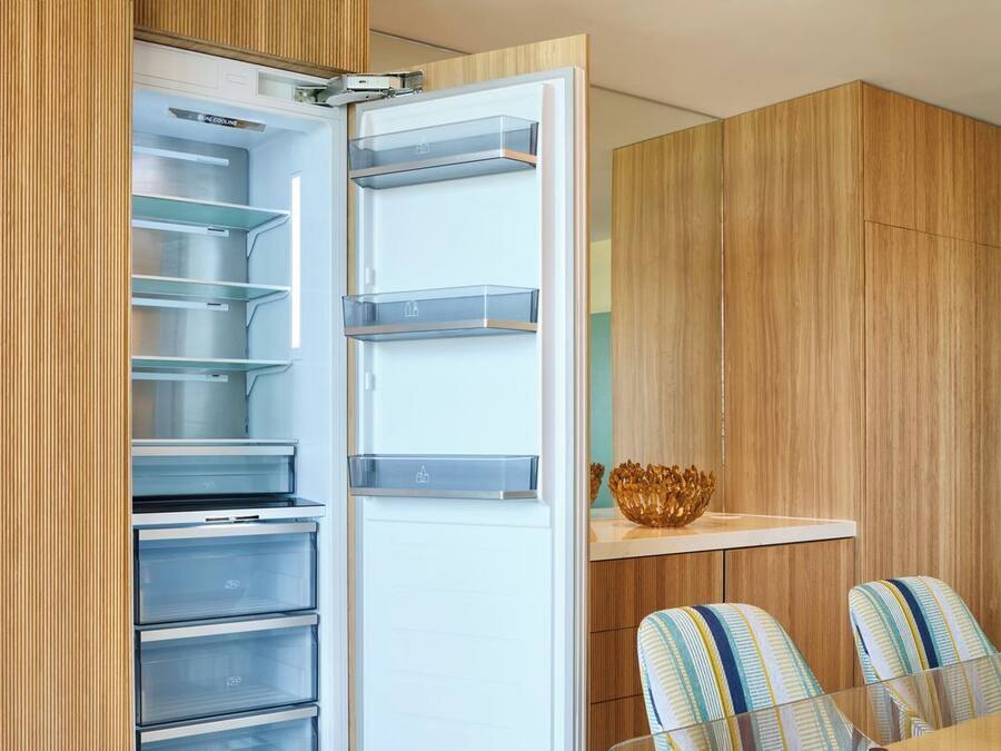 Eine moderne Küche mit integriertem Kühlschrank, übersichtlichen Regalen und einer Holzwandverkleidung.