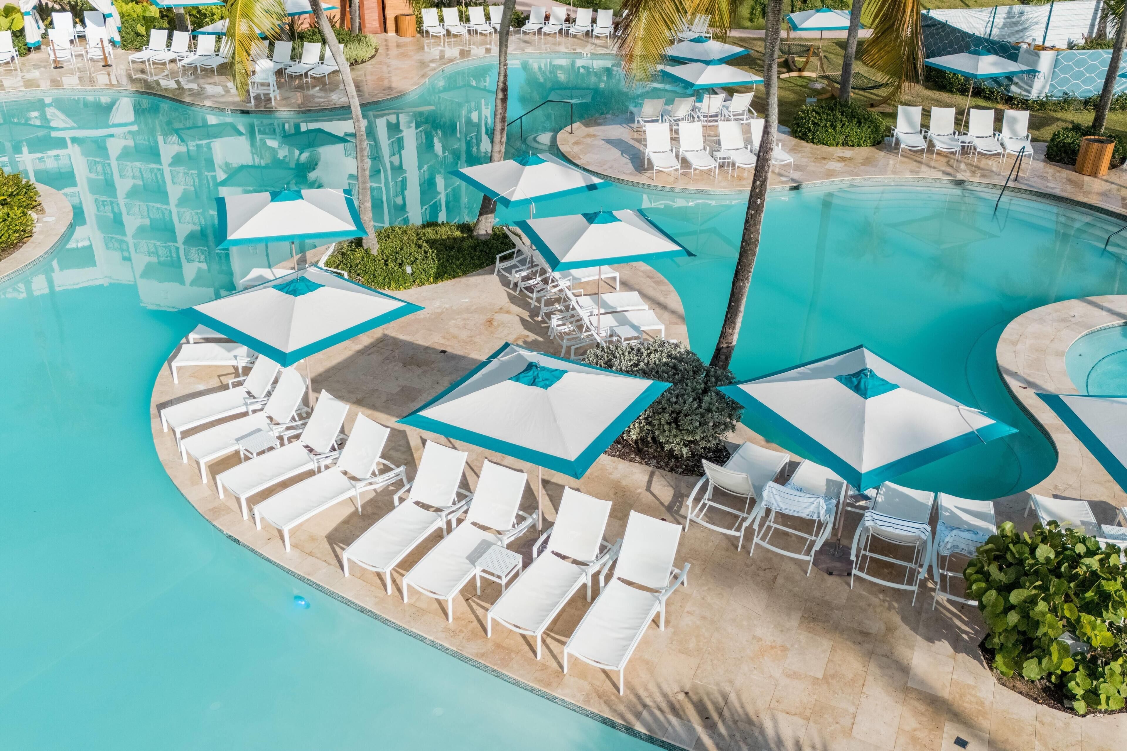 A pool area with multiple lounge chairs and umbrellas, surrounded by palm trees and greenery.