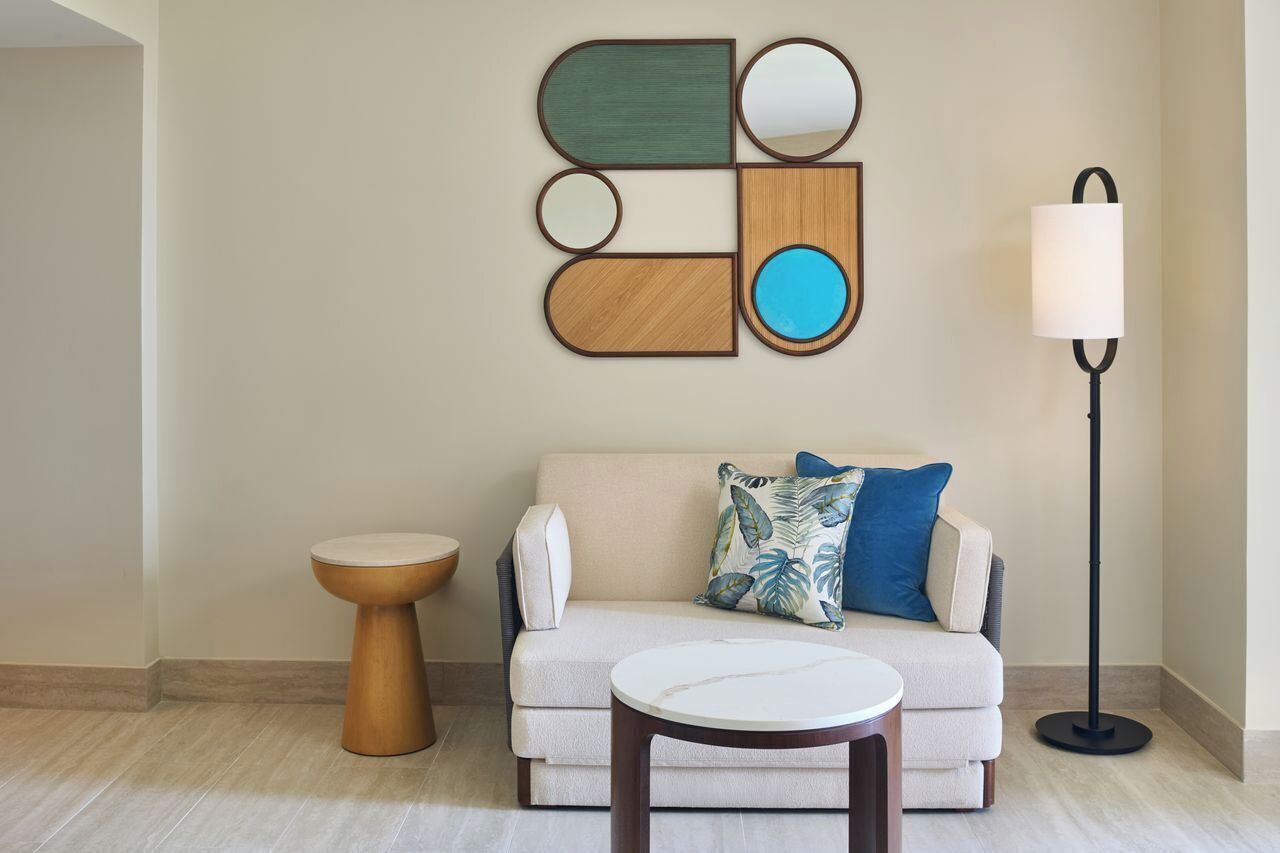 Un salon moderne avec un canapé beige, une table basse ronde, une table d’appoint en bois et un lampadaire.
