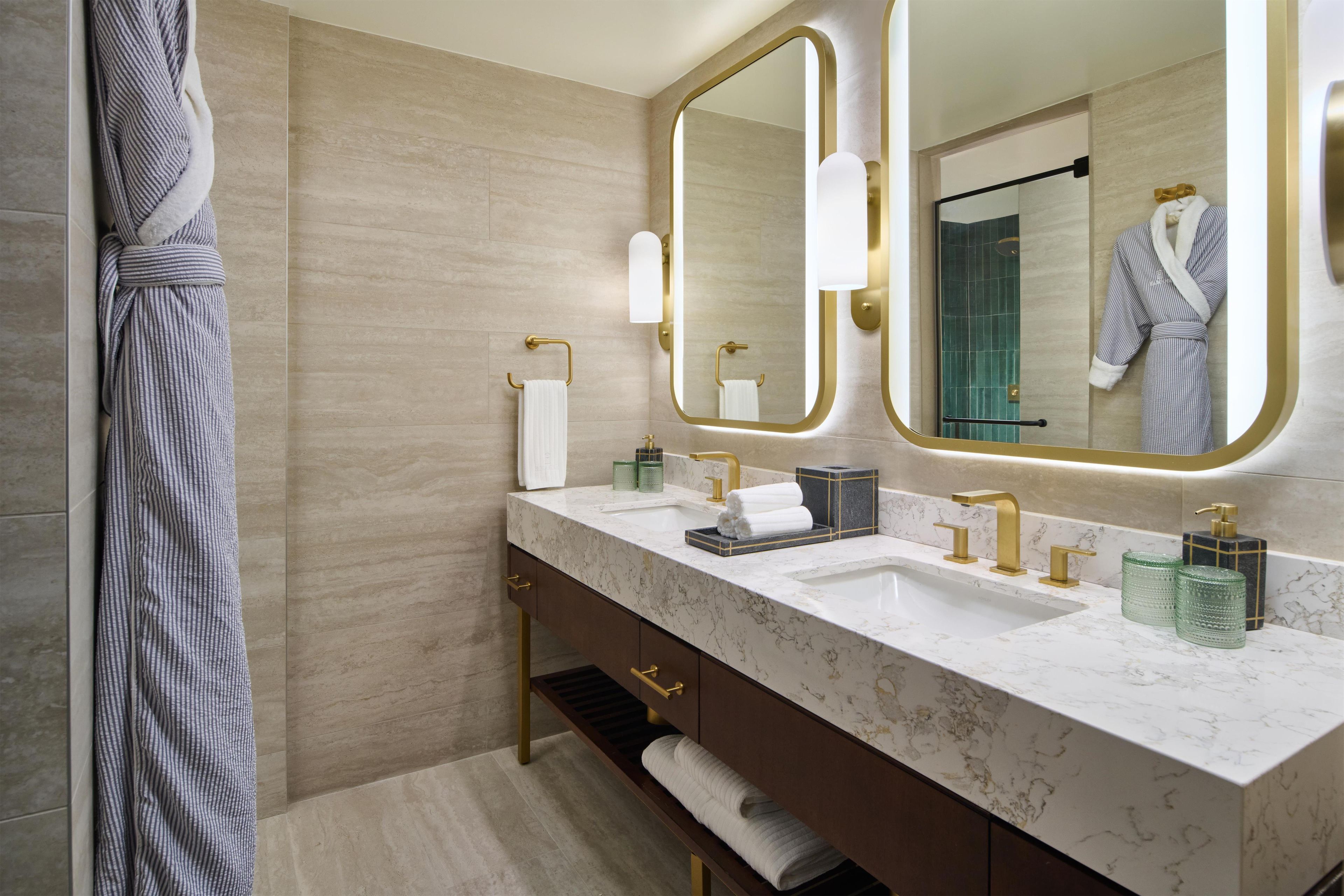 A modern bathroom with a marble vanity, gold fixtures, and a large mirror.