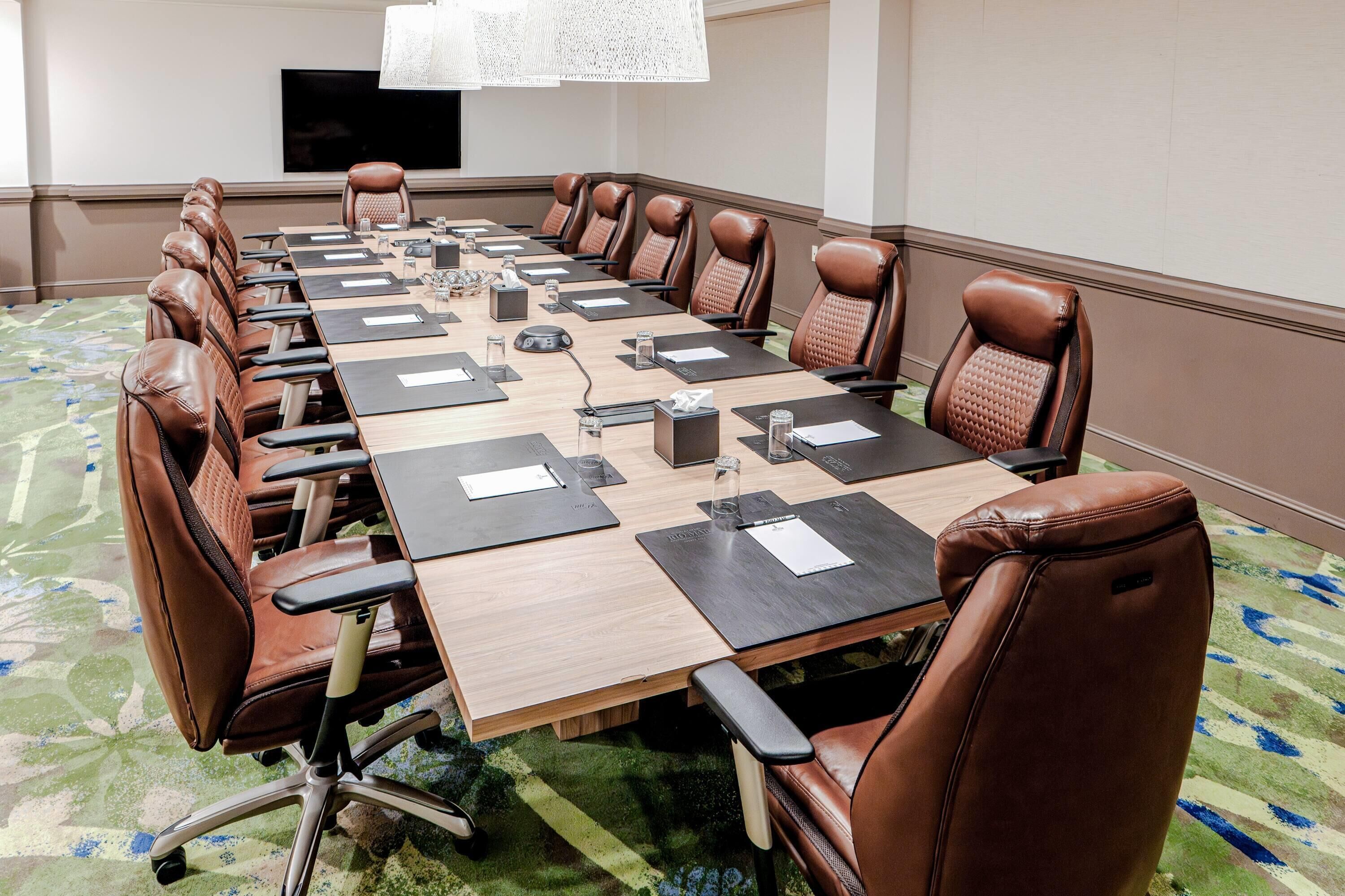 Una sala de conferencias con una mesa larga, sillas de cuero marrón y piso alfombrado.