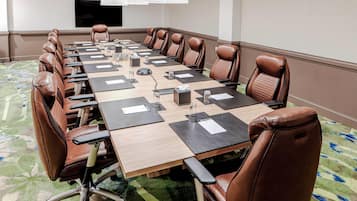 Una sala de conferencias con una mesa larga, sillas de cuero marrón y piso alfombrado.